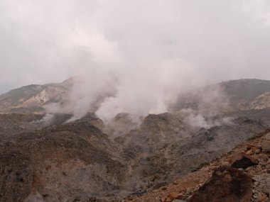 Tepesinden yükselen büyük bir duman bulutu olan bir dağ sırası. Duman yükseliyor ve gökyüzü bulutlu