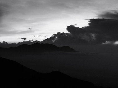 Karanlık bir gökyüzüne karşı bir dağ silueti var. Bulutlar alçak ve gökyüzü bulutlu