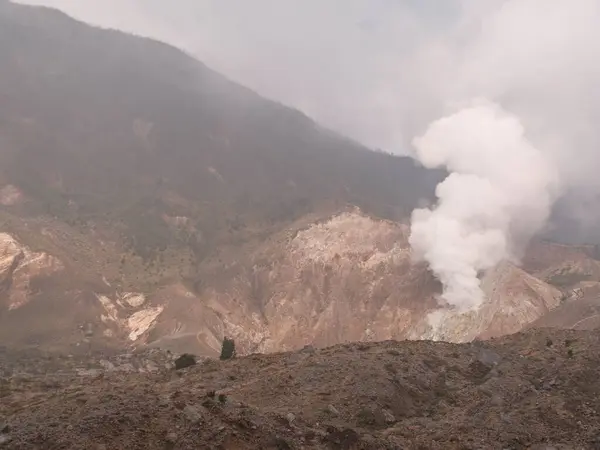 stock image A mountain with a volcano on top and a cloud of smoke rising from it. The scene is serene and peaceful, with the mountain providing a beautiful backdrop for the volcano