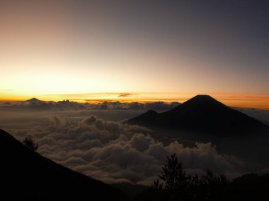 Güzel bir gün batımına karşı bir dağ silueti. Gökyüzü bulutlarla dolu ve güneş uzaklardan batıyor.