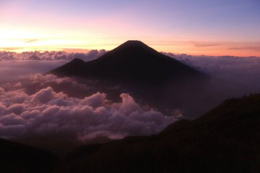 Güzel bir gün batımına karşı bir dağ silueti var. Gökyüzü bulutlarla dolu ve güneş batıyor.