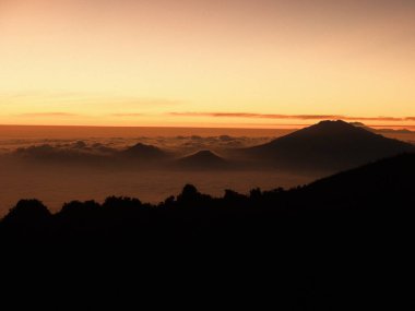 Güzel bir gün batımına karşı bir dağ silueti. Gökyüzü turuncu ve pembe renklerin bir karışımıdır. Huzurlu ve huzurlu bir atmosfer yaratır. Dağlar ağaçlarla çevrili.