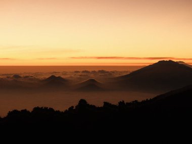 Güzel bir gün batımına karşı bir dağ silueti. Gökyüzü turuncu ve pembe renklerin bir karışımıdır. Huzurlu ve huzurlu bir atmosfer yaratır. Dağlar bulutlarla çevrili,