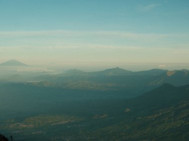 Arka planda mavi gökyüzü olan bir dağ silsilesinin bulanık görüntüsü. Dağlar ağaçlarla örtülmüş, gökyüzü ise berrak.
