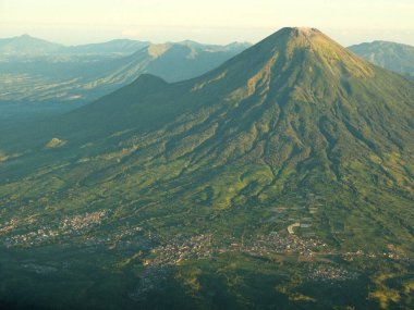 Yeşil bir yamacı ve uzak bir şehri olan bir dağ. Dağ ağaçlarla kaplı ve şehir küçük.