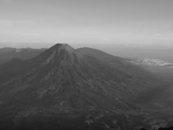 stock image A mountain with a black and white sky in the background. The mountain is covered in trees and he is a volcano