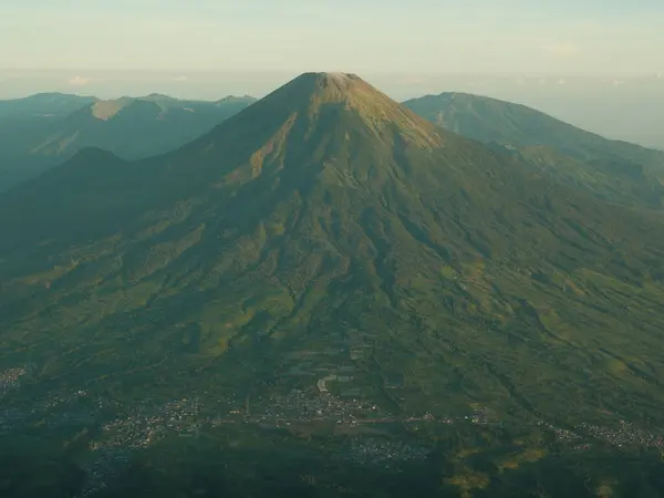 stock image A mountain with a green forest on top and a city below. The mountain is very tall and the city is small