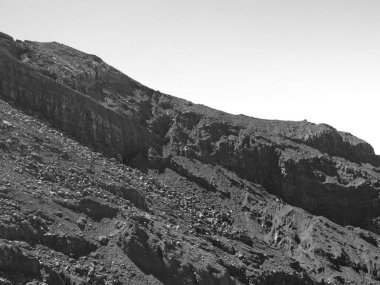 Arka planda gri gökyüzü olan kayalık bir yamaç. Tepe kayalar ve toprakla kaplı. Görünürde ne insan ne de hayvan var.