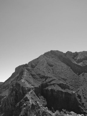 Arka planda açık mavi gökyüzü olan bir dağ. Dağ kayalık ve çoraktır.