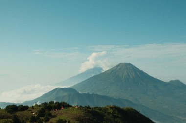 Ortasında volkan olan bir dağ sırası. Gökyüzü açık ve mavi