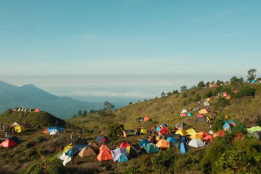 Bir tepenin yamacında büyük bir grup çadır kurulur, etrafında birçok insan toplanır. Sahne hareketli ve hareketli, her yaştan ve arka plandan insanlar dışarıda eğleniyor.