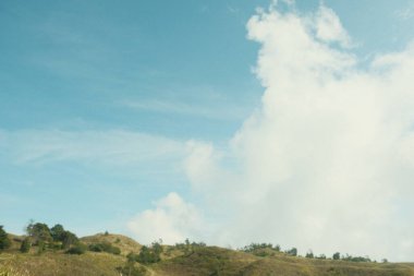 Bulutlu bir gökyüzünün bulanık bir görüntüsü ve arka planda birkaç ağaç var. Gökyüzü çoğunlukla mavi ve bazı beyaz bulutlar etrafa saçılmış.