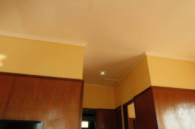 Odanın sarı bir duvarı ve kahverengi ahşap paneli var. Tavan beyaz ve oda sıcak, samimi.