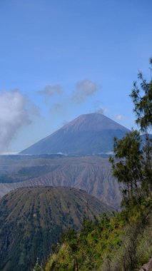 Ortasında büyük bir volkan olan bir dağ sırası. Gökyüzü açık ve mavi