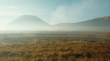 Sisli bir dağ sırası bir tarlanın arka planındadır. Gökyüzü mavi ve güneş gökyüzünde alçalır.