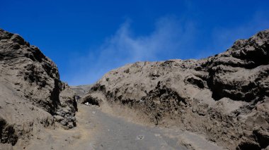 Arka planda mavi gökyüzü olan kayalık bir dağ. Gökyüzü açık ve güneş parlıyor.