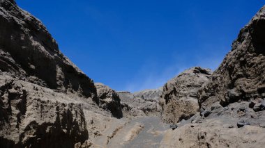 Üzerinde mavi gökyüzü olan kayalık bir kanyon. Gökyüzü berrak ve parlak, ve kayalar pürüzlü ve pürüzlü. Kanyonun uçsuz bucaksız genişliğiyle manzara huzurlu ve huzurlu.