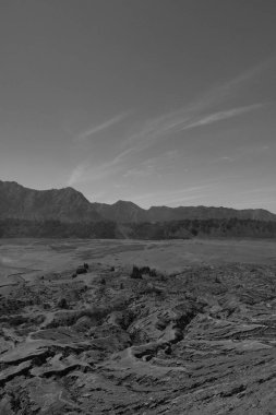 Arkasında dağ sıraları olan ıssız bir manzara. Gökyüzü açık ve güneş parlıyor.
