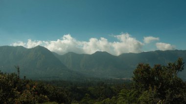 Dağlar ağaçlarla örtülmüş, gökyüzü de berrak. Manzara nefes kesici ve huzur verici. Gökyüzündeki bulutlar manzaraya derinlik ve boyut katıyor.