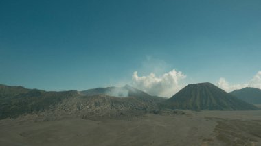 Uzakta volkan olan bir dağ sırası. Gökyüzü açık ve mavi. Volkan arka planda ve dağlar ön planda.