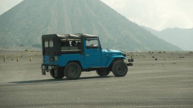 Büyük bir yanardağın önündeki toprak yolda mavi bir cip sürüyor. Jeep yoldaki tek araçtır ve yavaş sürüyordur. Sahne sessiz ve huzurlu.