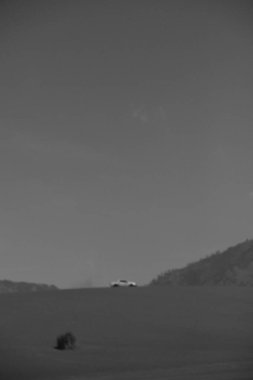 Bir araba çölde bir yolda gidiyor. Gökyüzü bulutlu ve güneş batıyor.