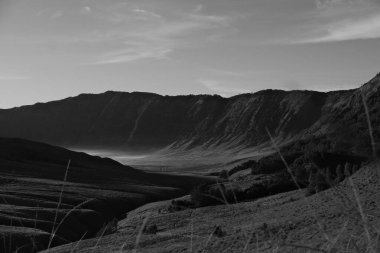 Arkasında dağ olan ıssız bir manzara. Gökyüzü bulutlu ve güneş batıyor.