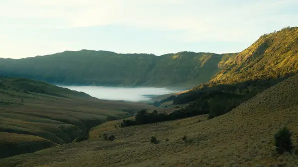 Stock image A mountain range with a foggy valley in the foreground. The valley is surrounded by trees and the mountains are covered in fog. The scene is peaceful and serene, with the fog adding a sense of mystery