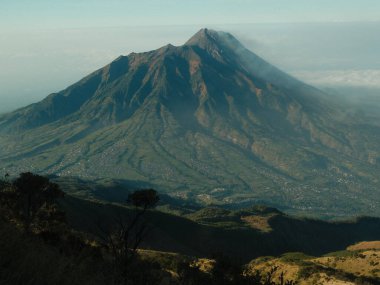 Uzakta bir şehri olan bir dağ. Dağ ağaçlarla kaplı ve şehir arka planda.