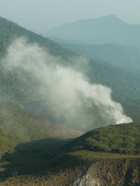 Tepesinden yükselen büyük bir duman bulutu olan bir dağ sırası. Duman yükseliyor ve gökyüzü bulutlu