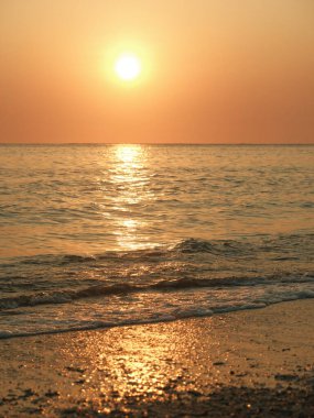 Güneş okyanusun üzerinde batıyor, suyun üzerine sıcak bir parıltı saçıyor. Gökyüzü turuncu ve pembe renklerin bir karışımıdır. Huzurlu ve huzurlu bir atmosfer yaratır. Dalgalar yavaşça kıyıya vurur