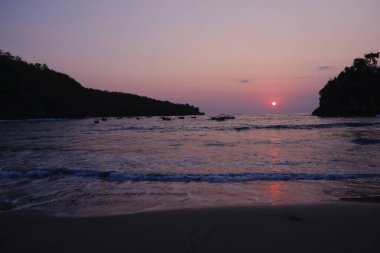 Okyanusun üzerinde güzel bir günbatımı ve suda birkaç tekne. Gökyüzü turuncu ve pembe renklerin bir karışımıdır. Huzurlu ve huzurlu bir atmosfer yaratır. Tekneler suyun her tarafına dağılmış.