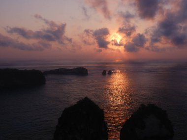 Önünde birkaç kayayla okyanusun üzerinde güzel bir günbatımı. Gökyüzü turuncu ve pembe renklerin karışımıdır. Huzurlu ve huzurlu bir atmosfer yaratır.