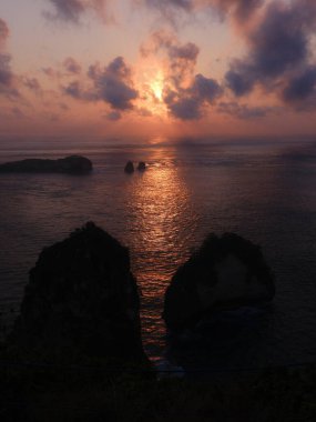 Güneş okyanusun üzerinde batıyor, suyun üzerine sıcak bir parıltı saçıyor. Gökyüzü bulutlarla dolu. Huzurlu ve huzurlu bir atmosfer yaratıyor.