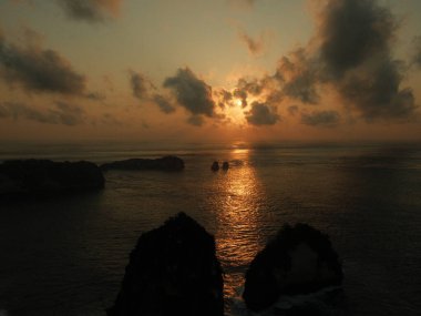 Güneş okyanusun üzerinde batıyor, suyun üzerine sıcak bir parıltı saçıyor. Gökyüzü bulutlarla dolu. Huzurlu ve huzurlu bir atmosfer yaratıyor.