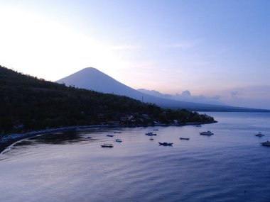 Arkasında dağ olan güzel mavi bir okyanus. Su sakin, gökyüzü mavi ve mor karışımı.