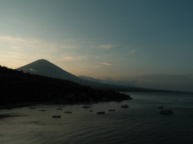 Arka planda karanlık bir gökyüzü ile bir dağ sırası görülebilir. Su sakin ve üzerinde yüzen bir sürü tekne var.