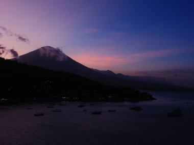 Mor gökyüzüne karşı bir dağ silueti var. Dağlar bulutlarla kaplı ve gökyüzü koyu mor