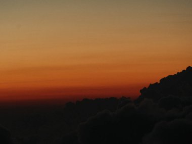 Arka planda dağ olan gün batımının bulanık bir fotoğrafı. Gökyüzü turuncu ve bulutlar beyaz
