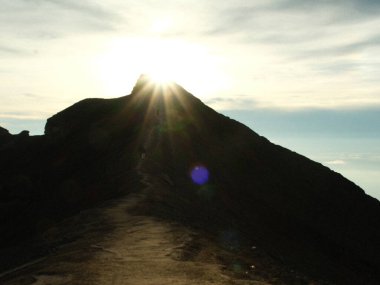 A mountain with a sun shining on it. The sky is cloudy and the sun is in the middle of the sky clipart