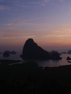 Güzel bir gün batımına karşı bir dağ silueti var. Gökyüzü turuncu ve mor renklerin bir karışımıdır. Huzurlu ve huzurlu bir atmosfer yaratır. Dağın varlığı ihtişam katıyor