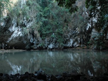 Kayalar ve ağaçlarla çevrili büyük bir su kütlesi. Su sakin ve hareketsizdir. Çevredeki manzarayı yansıtır. Huzurlu ve huzurlu bir sahne.