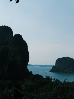 Arka planda dağlar olan güzel bir su kütlesi manzarası. Dağlar yüksek ve kayalık, su sakin ve berrak. Gökyüzü mavi ve görünürde hiç bulut yok.