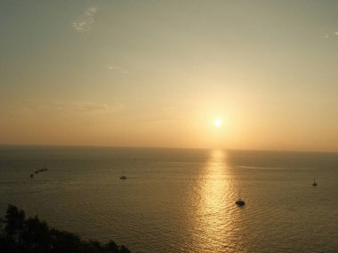 Güneş okyanusun üzerinde batıyor, suyun üzerine sıcak bir parıltı saçıyor. Gökyüzü turuncu ve pembe renklerin bir karışımıdır. Huzurlu ve huzurlu bir atmosfer yaratır. Uzakta.