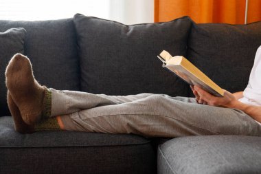 Kanepede oturup kitap okuyan bir adam.