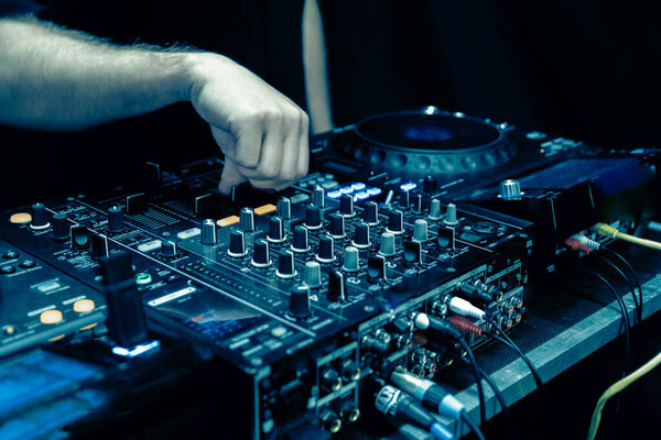 Закройте руки ди-джея на диджейской консоли, играющей музыку вечеринки
