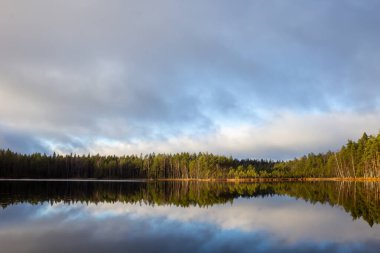 Finlandiya 'da güzel bir göl manzarası. Su gökyüzünü ve ormanı yansıtıyor.