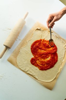Çiğ pizza hamuruna domates sosu sürüyorum.
