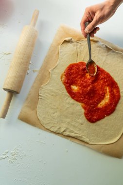 Çiğ pizza hamuruna domates sosu sürüyorum.