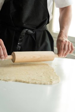 Eller hamuru pişirirken beyaz masa üzerinde merdaneyle